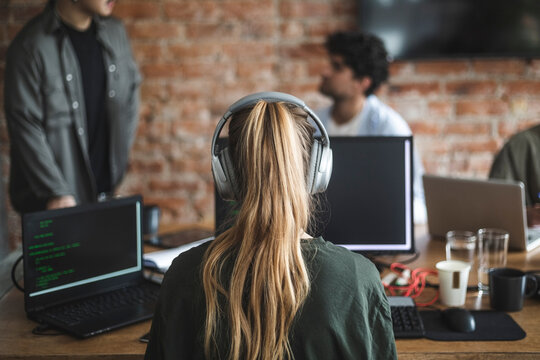 Female hacker with headphones working over computer in office