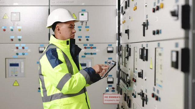 Asian man electrical engineer hold tablet monitoring electrical system in control room. Technician inspect to control panel screen system for generate electricity of factory in manufacture industrial
