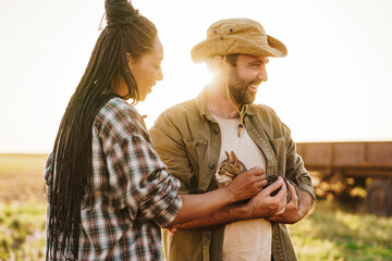Multiracial man and woman holding cat while working on farm