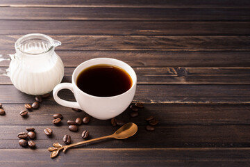 A cup of coffee with milk or cream is placed on a dark wooden floor.