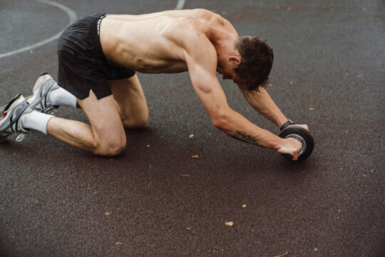 Young shirtless sportsman doing push-ups with equipment on playground