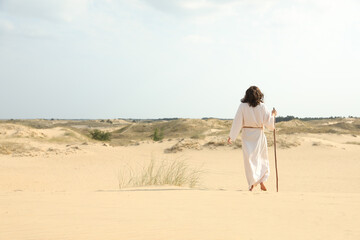 Jesus Christ walking with stick in desert, back view. Space for text