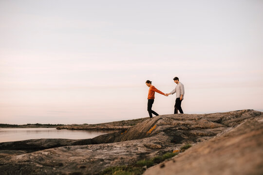 Gay couple holding hands while walking at lakeshore against sky