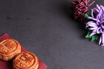 Chinese moon cake and the chrysanthemum is a symbol of autumn on a dark gray background. Asian traditional mid-autumn festival. Translation of hieroglyphs: mango, pomegranate and lotus.