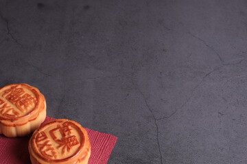 Chinese moon cake on a dark gray background. Asian traditional mid-autumn festival. Translation of hieroglyphs: mango, pomegranate and lotus.