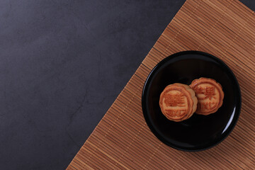 Chinese moon cake on a dark gray and bamboo background. Asian traditional mid-autumn festival. Translation of hieroglyphs: mango, pomegranate and lotus.
