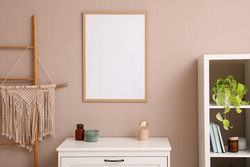 Empty frame hanging on pale rose wall over chest of drawers in room. Mockup for design
