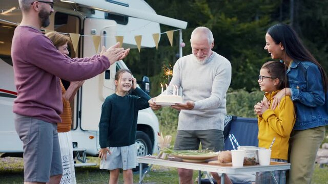 Multi-generation family celebrating birthday outdoors at campsite, caravan holiday trip.