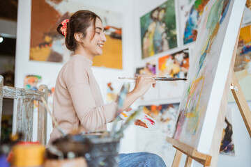 asian female artist painting on canvas doing art projects on her studio