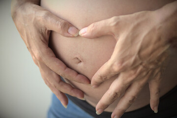 Hands in a form of a heart on a belly of a pregnant woman