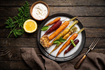Fototapeta na wymiar Roasted young whole colorful carrot with herbs served on plate over wooden background. Top view