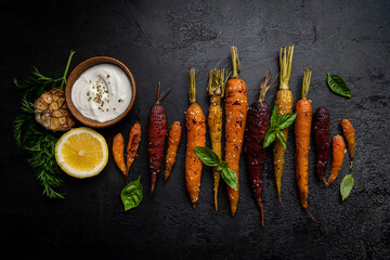 Roasted young whole colorful carrot with herbs over black background. Top view