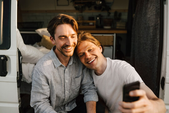 Smiling male friends taking selfie on mobile phone at doorway of camping van