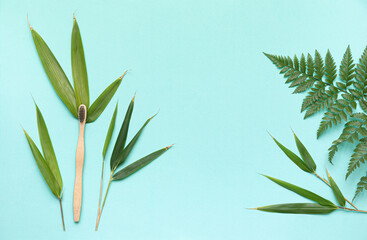 Bamboo toothbrush on a table with copy space on a blue background. Styled composition of flat lay with bamboo leaves .