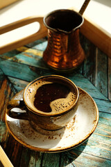 Freshly brewed hot turkish coffee in ceramic espresso cup. Copper cezve. Turquoise wooden tray. Daylight, shadows.
