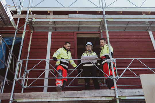 Female building contractor discussing over floor plan with male colleagues at scaffolding