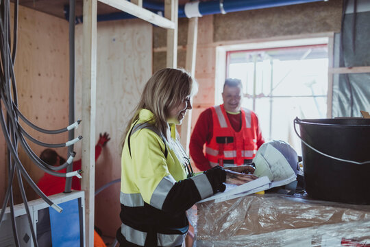 Smiling female building contractor analyzing floor plan while discussing with male colleague at construction site