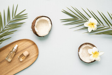 Obraz na płótnie Canvas Coconut essential oil and palm leaf oil on a table with copy space on a pastel background. Styled composition of flat lay with tropical leaves and flowers.