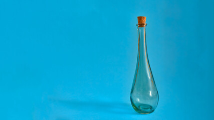 Empty glass bottle with original shapes on a solid neutral colored background.