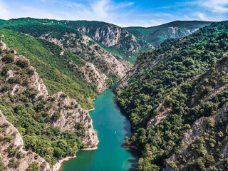 Drone view of Matka Canyon. Drone shot of a lake in a canyon in North Macedonia. Rocky green slopes. Transparent water surface of the lake. Mountain trail along the river. Lake in the mountains