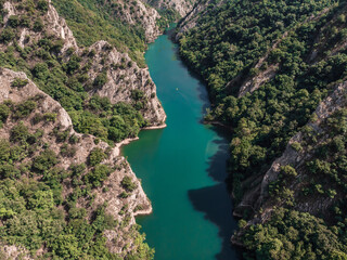 Obraz premium Drone view of Matka Canyon. Drone shot of a lake in a canyon in North Macedonia. Rocky green slopes. Transparent water surface of the lake. Mountain trail along the river. Lake in the mountains