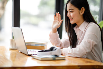 Young asian woman having conference video call using laptop talking to coworker online audience sitting at office desk in evening.	
