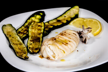 mediterranean dish with roasted squid and zucchini and lemon, on black background