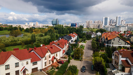 Panoramic view of a new neighborhood cottage village in the foreground and the modern building of national library of Belarus in the background. Dramatic sky background.