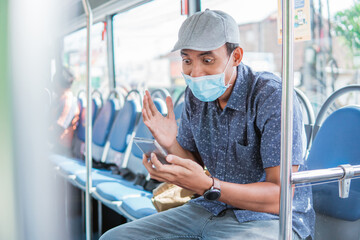 Naklejka na ściany i meble Happy asian man cheering celebrating looking at smartphone while in public bus with mask