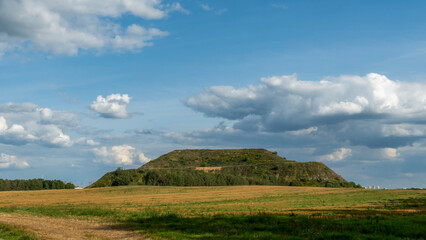 Obraz premium Closed city dump. Restoration of the territory. Landscaping of a large hill of garbage. In the background is a metropolis and a blue sky with clouds. Ecological problem.