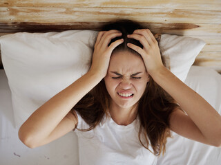 woman lies in bed with closed eyes and holds her head discontent