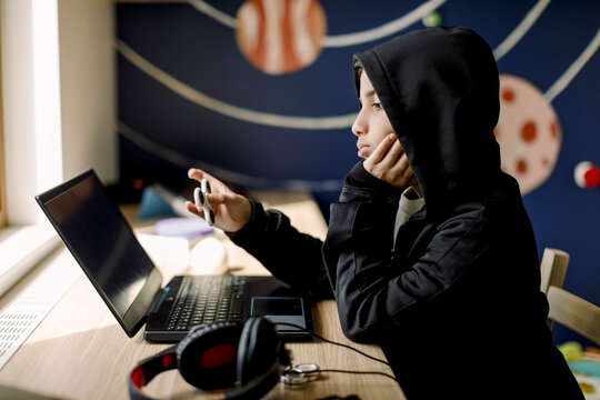 Autistic boy with hand on chin looking at laptop in bedroom