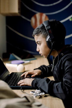 Pre-adolescent boy playing game on laptop in bedroom