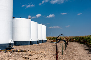 crude oil storage tanks with secondary containment and fencing in a rural corn field