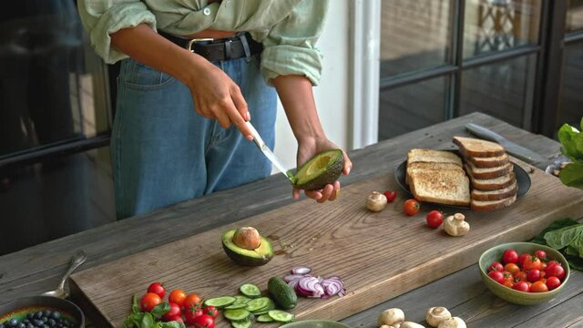 woman hands slicing green avocado on the wood board for preparing vegan full grain toast with mushrooms and vegetables outdoor on terrace healthy food concept 4K