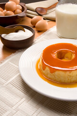 Pudim de leite condensado com calda de caramelo e ingredientes sobre mesa com produção.