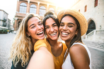 Three young women taking selfie portrait on city street - Multicultural female friends having fun...