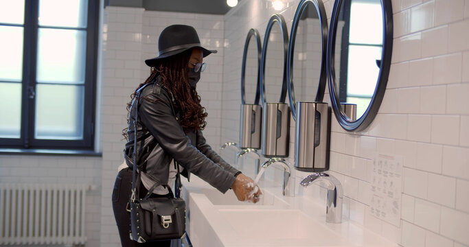 Side view of african woman in safety mask washing hands in public toilet