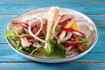 Chicken fajitas with grilled onions and bell peppers and tortillas on blue wooden table