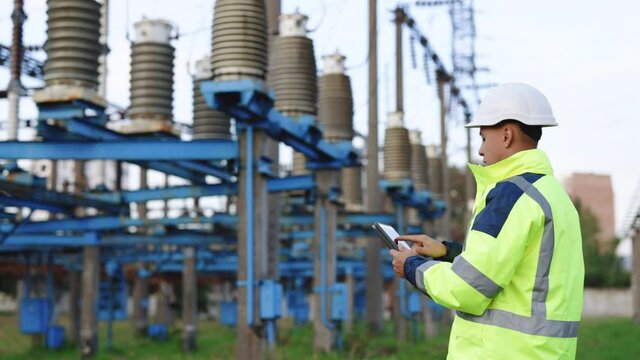 Electrical worker engineer a working with digital tablet, power near tower with electricity. Energy business technology industry concept. Electrical engineer studying reading on tablet.