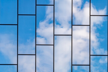 Reflection of blue sky with white clouds in windows of modern office building. Glass building with cloudy blue sky background.