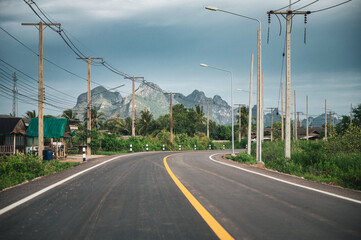 Asphalt road with mountain range and utility pole and lamppost in countryside at Sam Roi Yot