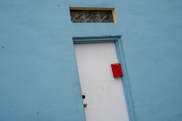 Closeup view at angle of blue painted building exterior with door and red mailbox, small glass window above. 