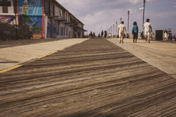 Long angle view of beach boardwalk, buildings and people walking in distance. 