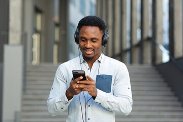 young african student listening to music from smartphone using big headphones, smiling from the convenience of using the app