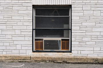 Closeup of basement window with old dilapidated air conditioner, surrounded by brick wall detail. 