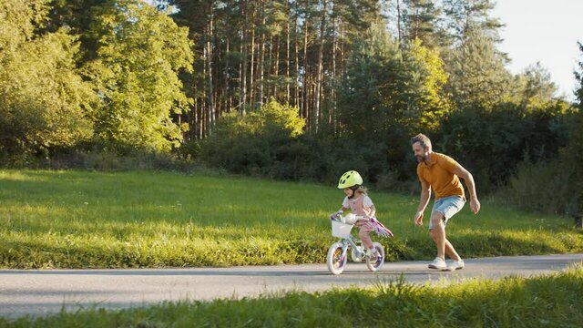 Side view of father teaching his daughter how to ride a bike.