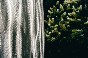 Side by side shot of metallic wall surface in focus foreground, flowering tree to right in background, slightly blurry. 