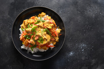 Thai breakfast Gai Pad Pongali with chicken, eggs, spicy, yellow thai curry paste,tomato, rice in black bowl made in wok. Close up. Pan-Asian cuisine. Thai Food Stir Fried.