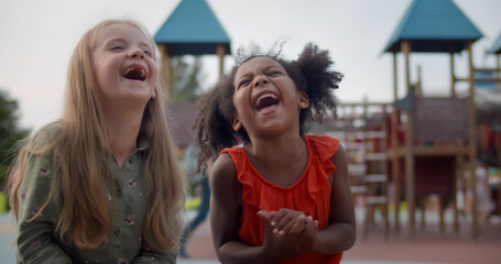Medium shot of adorable diverse little girls laughing and sitting on bench outdoors